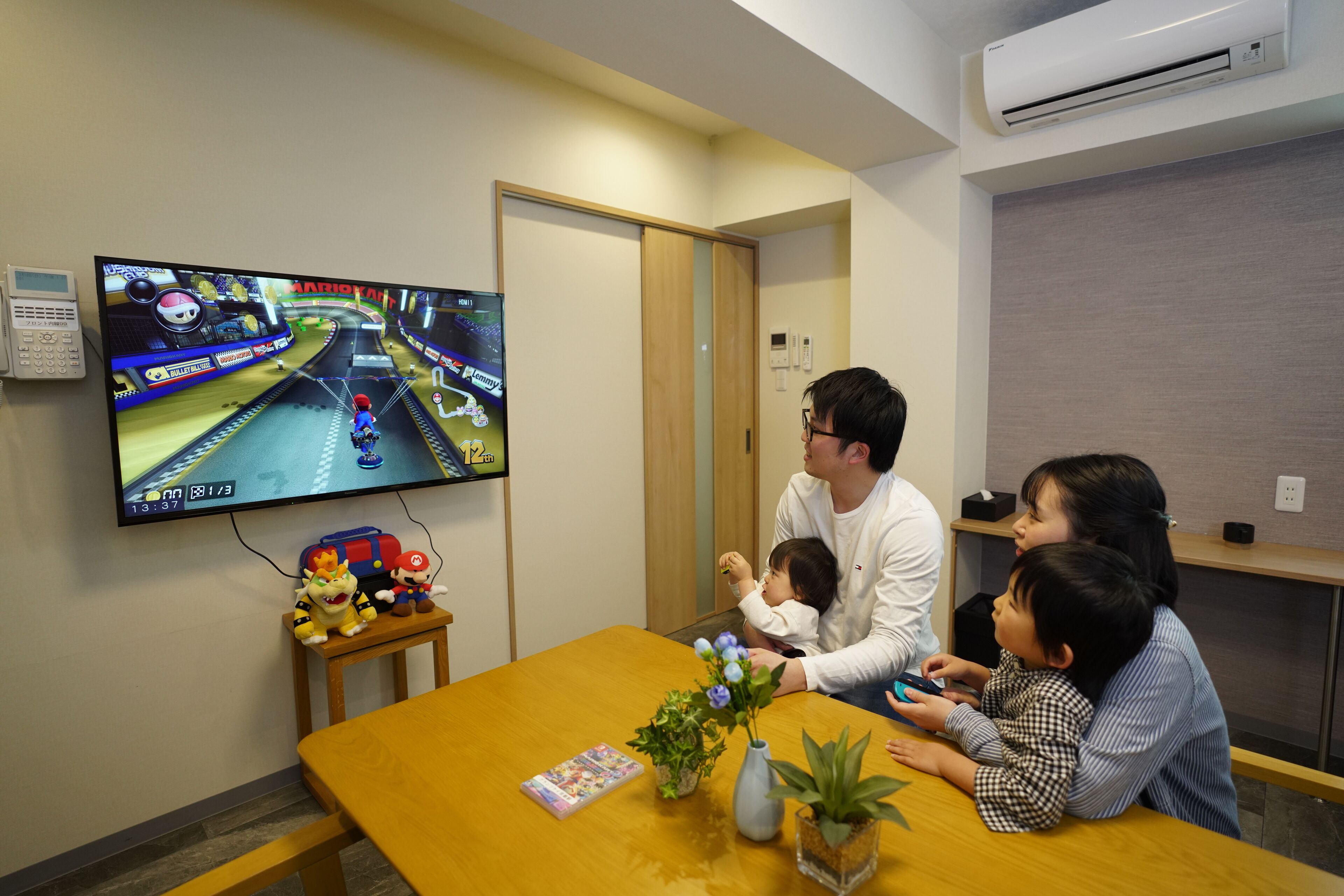 A room with a television displaying a video game, a wooden table, a small plant, and a toy.
