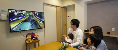 A room with a television displaying a video game, a wooden table, a small plant, and a toy.