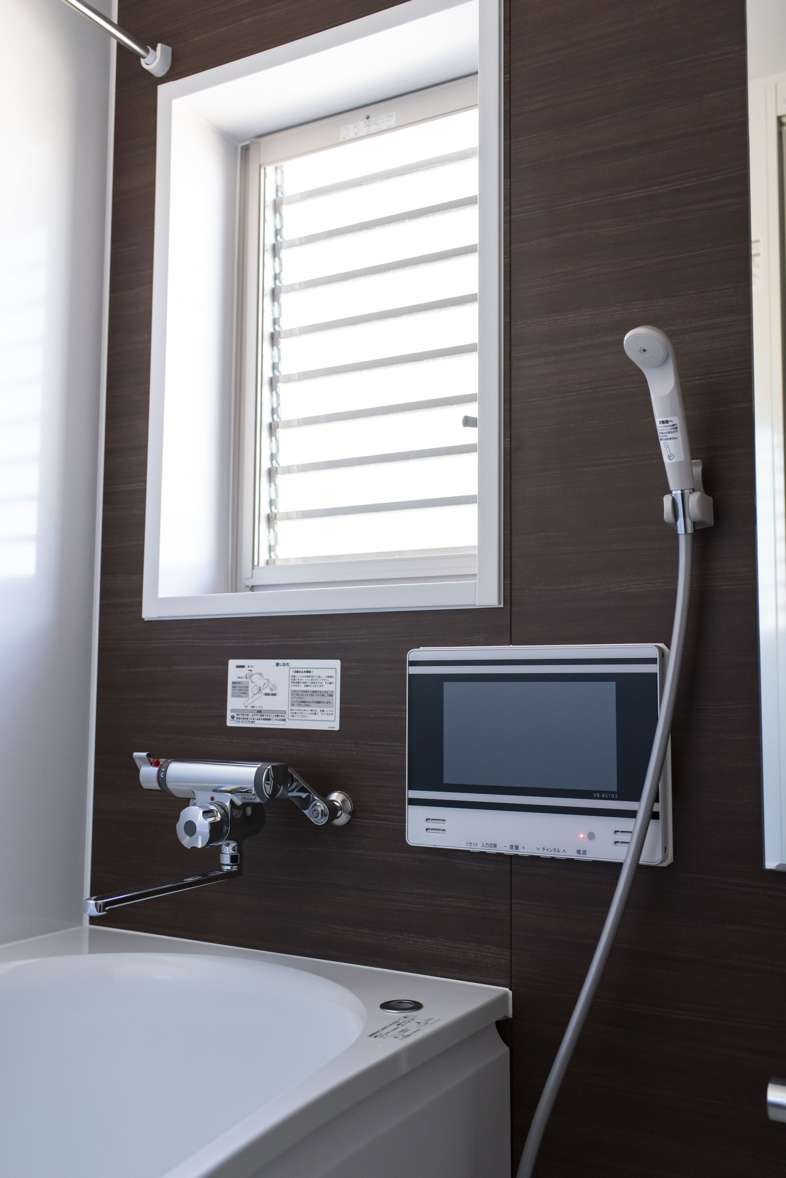 Ein Badezimmer mit Fenster, einer digitalen Bedienkonsole und einer Duschbrause.