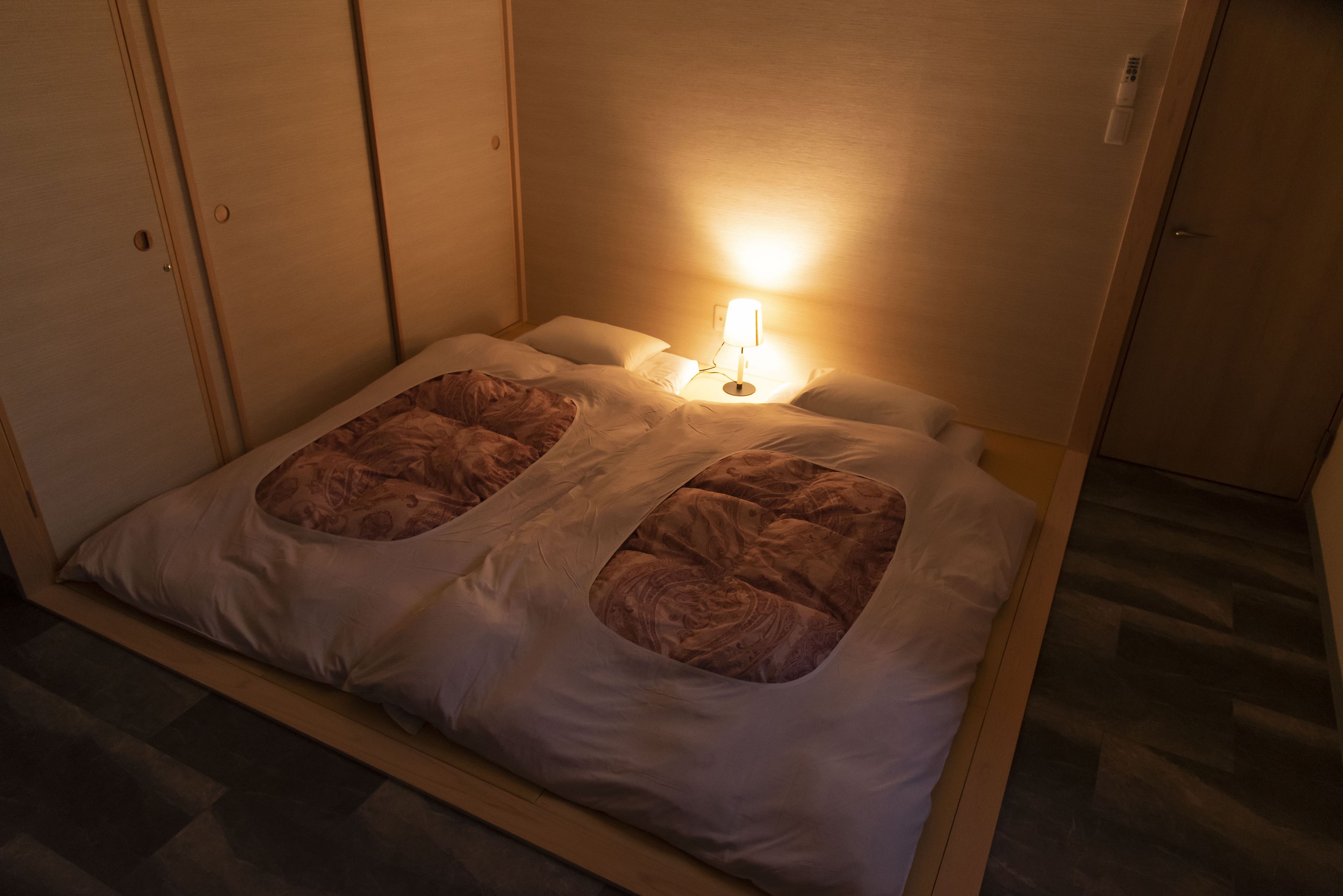 Una cama individual con cabecera, una lámpara de noche y suelo de madera.