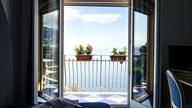 A balcony with a view of the sea, two potted plants, and a chair. - Hotel Villa Pandora (Maiori)