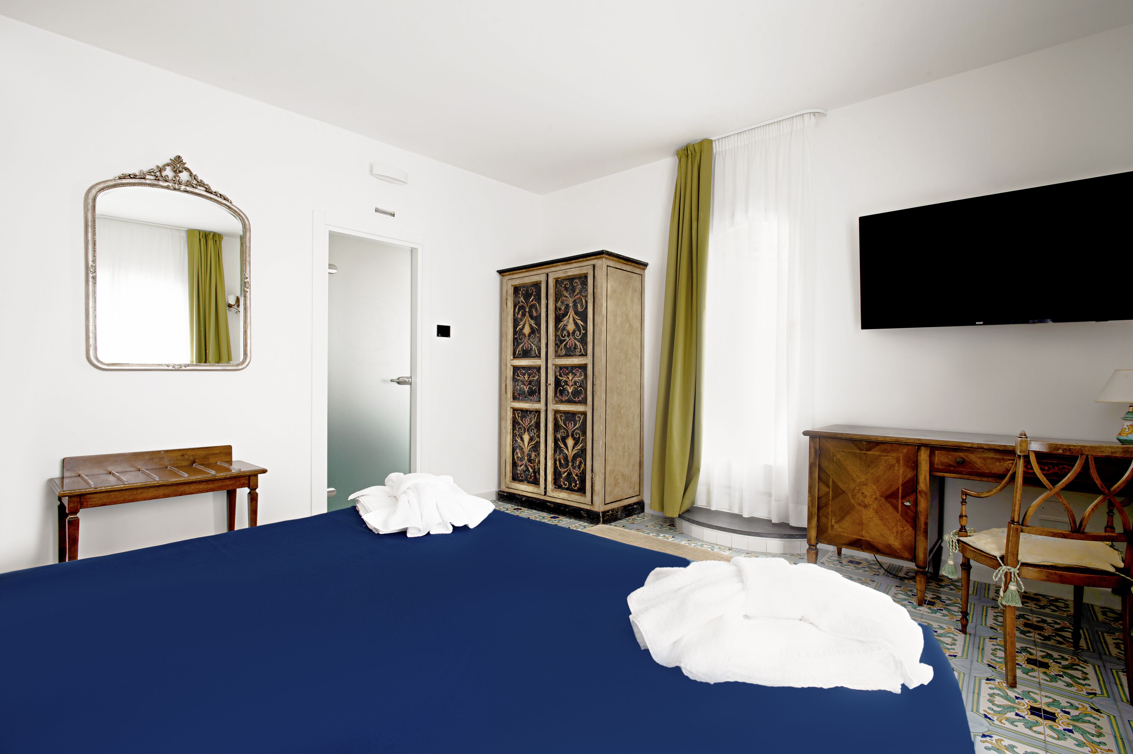A hotel room with a large bed, a wooden cabinet, a television, and a desk.