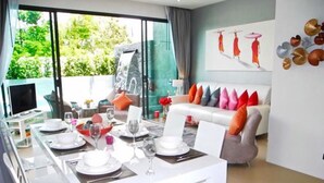 Un comedor con una mesa blanca dispuesta para cuatro personas, un sofá con cojines de colores, y vistas a una cascada y follaje exterior.