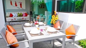 Un espacio de comedor al aire libre con una mesa dispuesta para cuatro personas, rodeado de sillas de mimbre con cojines naranja.