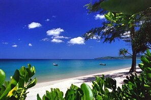 Une plage à l’eau turquoise et limpide, avec deux bateaux et une rive sablonneuse bordée de végétation.
