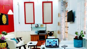 Een woonkamer met een plafondventilator, een televisie, een laptop op een tafel en een rode en witte muur met decoratieve details.