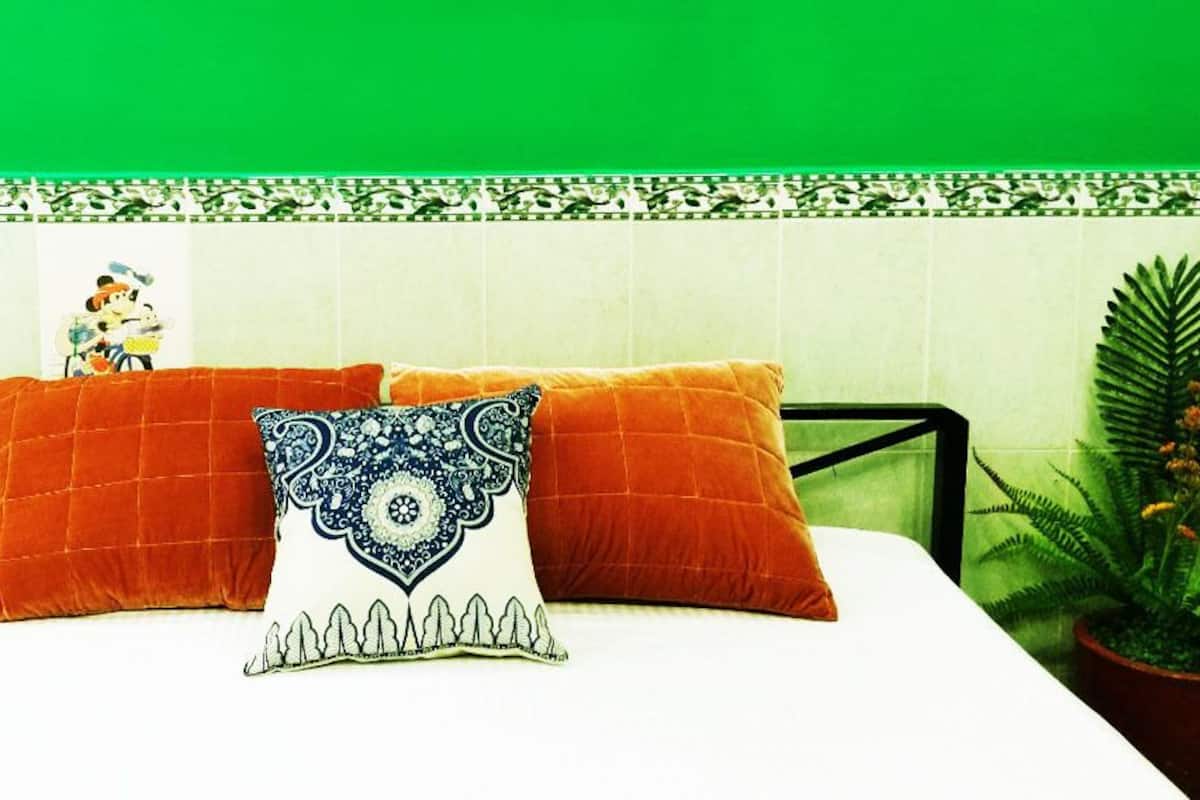 Cama com duas almofadas laranja e uma almofada decorativa com padrão azul e branco.