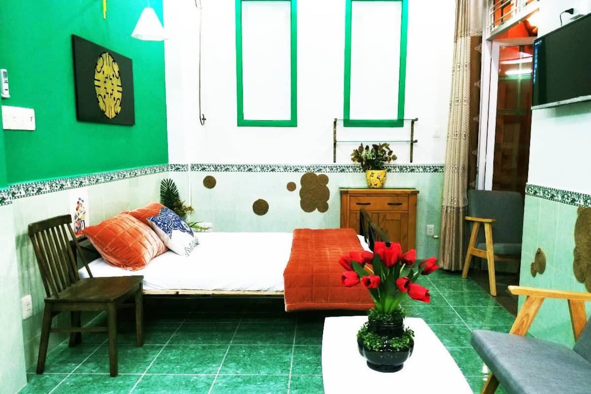 Quarto com cama, cadeira, mesa pequena com planta e televisão.