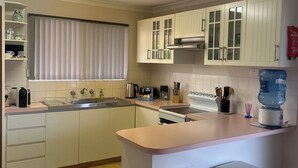 A modern kitchen with white cabinets, a central island with bar stools, a built-in oven, and a water dispenser. - Sharpie’s Family Shack 🏝 Greenhead.   ☀️ Free Wi-Fi (Green Head)