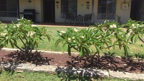 A two-story house with a tiled roof, a front porch with chairs, and a small garden with flowering plants. - Sharpie’s Family Shack 🏝 Greenhead.   ☀️ Free Wi-Fi (Green Head)