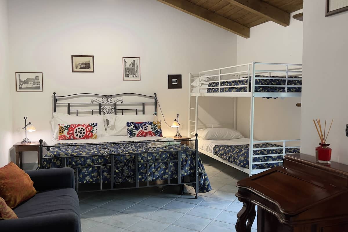 A bedroom with a bunk bed, a single bed, a desk, a chair, and two bedside tables with lamps.