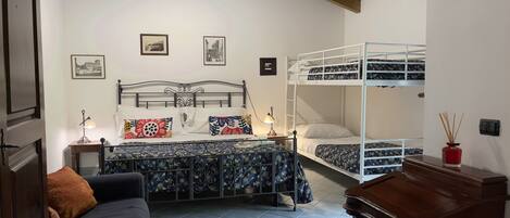 A bedroom with a bunk bed, a single bed, a desk, a chair, and two bedside tables with lamps.