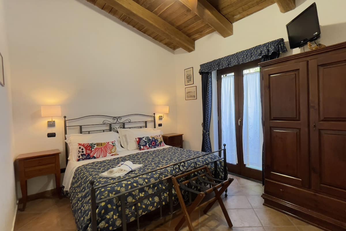 A bedroom with a bed, two bedside tables, a wardrobe, a television, and a window with curtains.