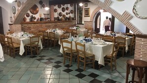 Un restaurante con varias mesas dispuestas para comer, una pared de ladrillo con macetas colgantes y un suelo de baldosas.