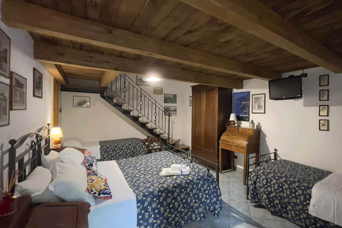 A bedroom with two beds, a desk, a chair, a TV, and a staircase.