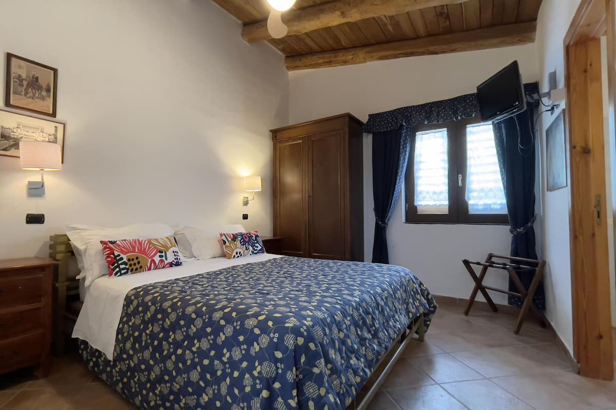 A bedroom with a bed, wooden wardrobe, a desk, and a window with curtains.