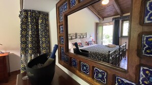 Un dormitorio con un espejo grande, una cama con ropa de cama estampada y una mesita de noche con una botella y vasos.