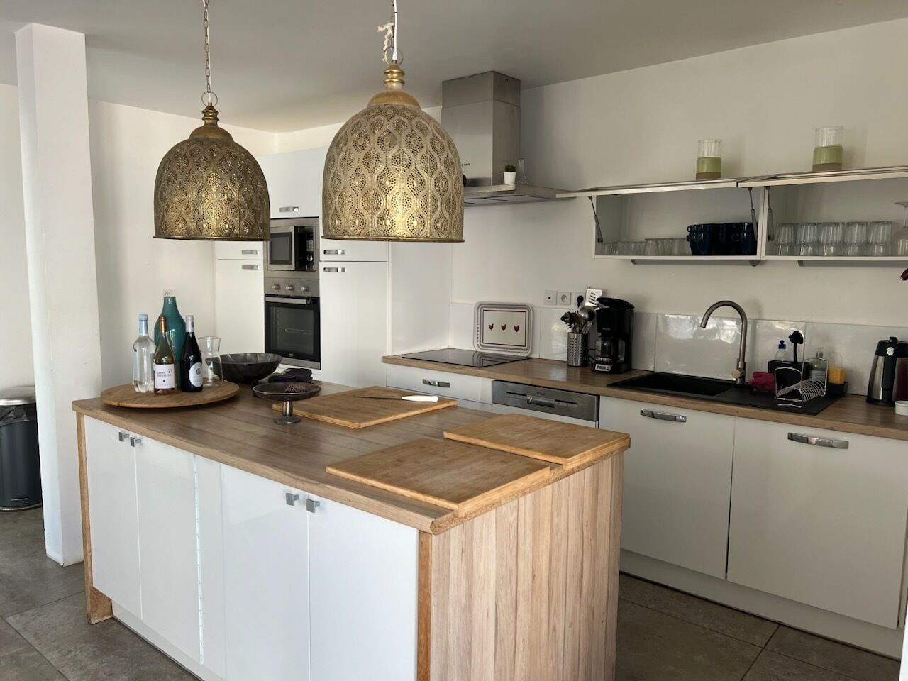 Une cuisine moderne avec un îlot central en bois, des luminaires suspendus, un four à micro-ondes et un évier.
