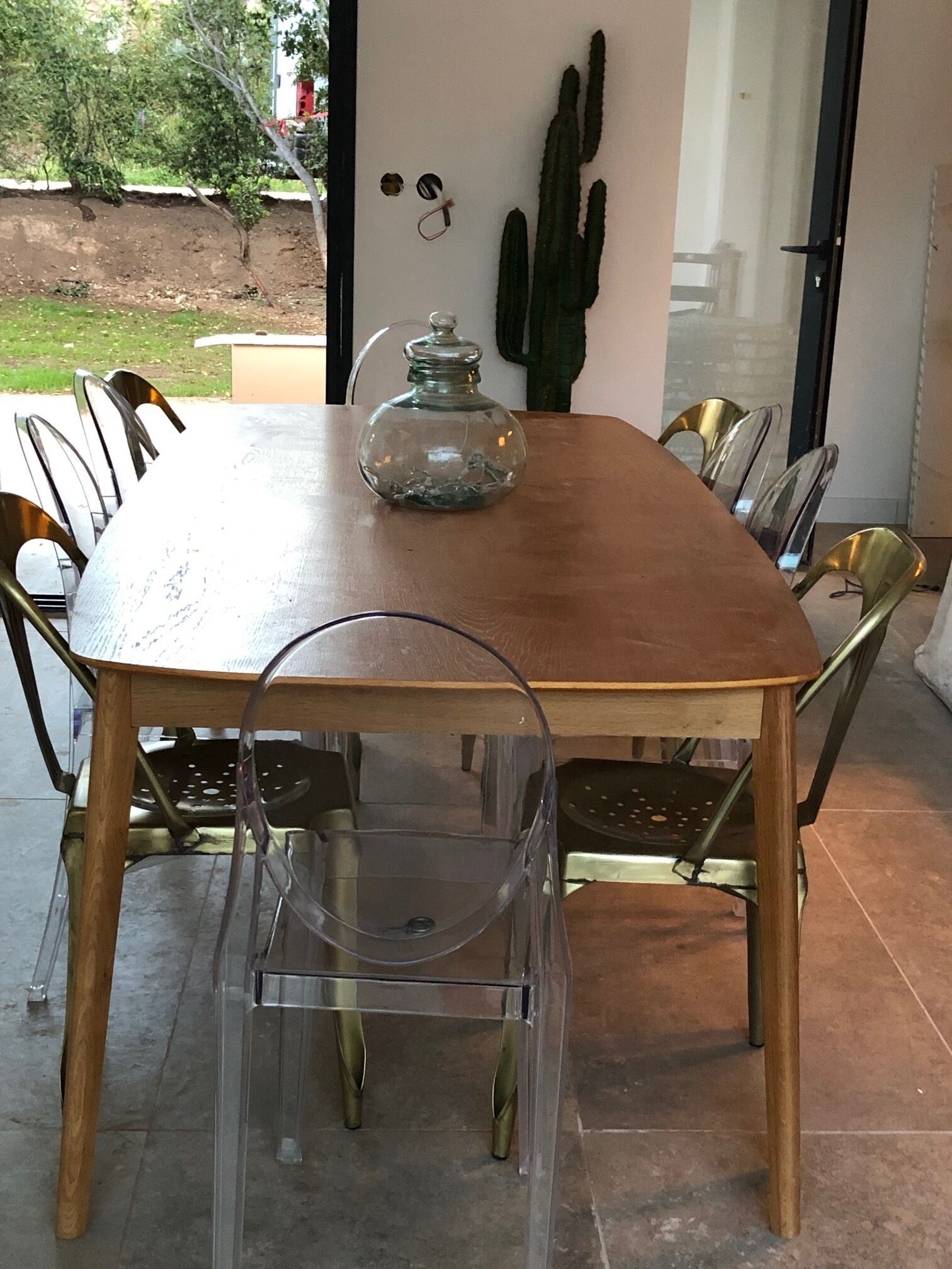Une table à manger agrémentée d’un vase en verre servant de centre de table, entourée de chaises transparentes et décorée d’un cactus.