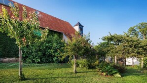 Un bâtiment doté d’un toit recouvert de tuiles rouges, d’une tour et d’un jardin bien entretenu, avec des arbres et de la pelouse.