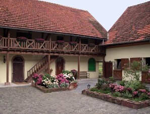 Traditional building with a red-tiled roof and a balcony, set amidst a stone-paved courtyard with flower beds and a lantern.
