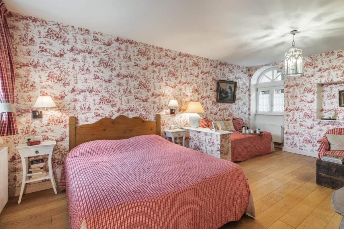 Une chambre à coucher avec un papier peint à motifs floraux, un lit en bois, des tables de chevet, des lampes et une fenêtre donnant sur un beau paysage.