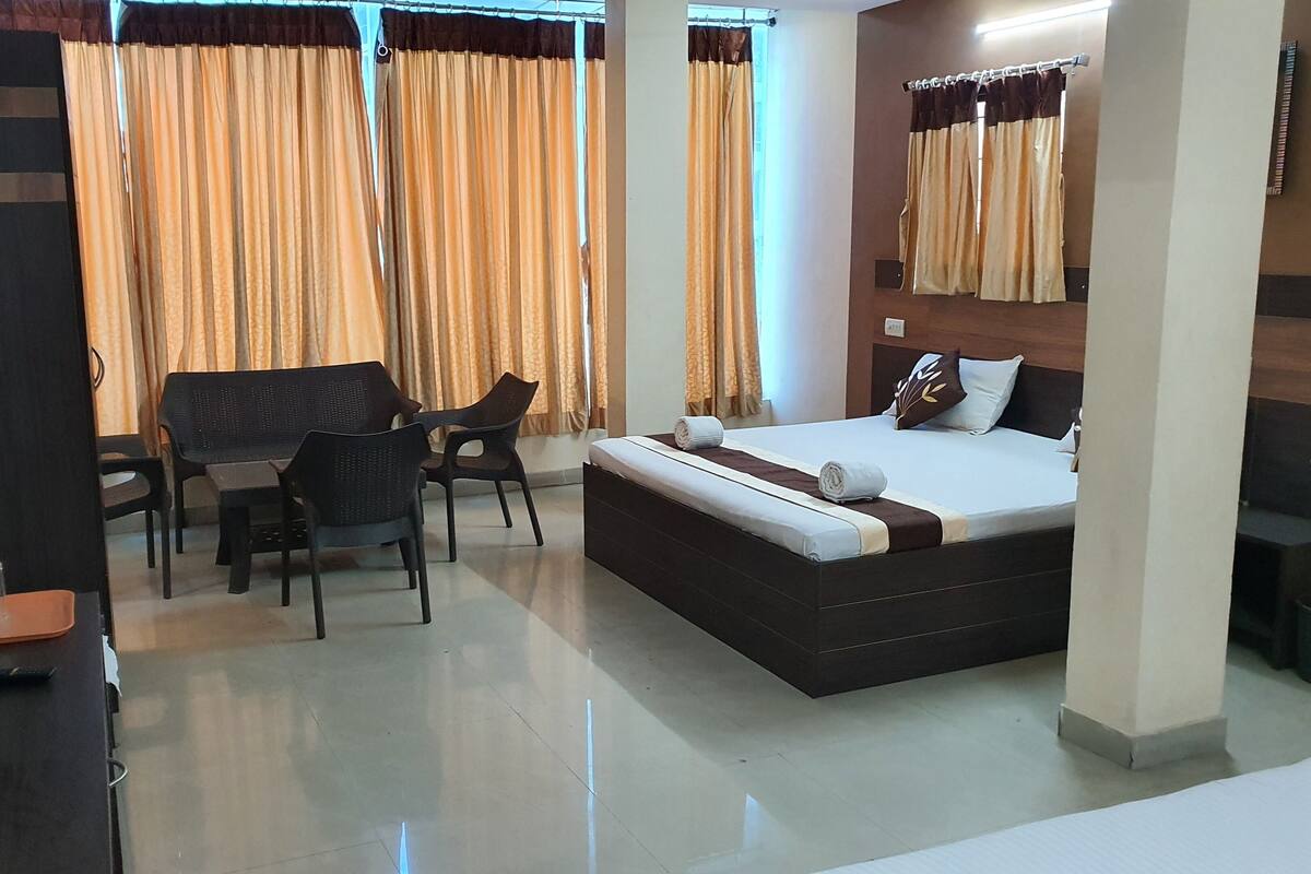 A hotel room with a bed, a desk, two chairs, a TV, and curtains.