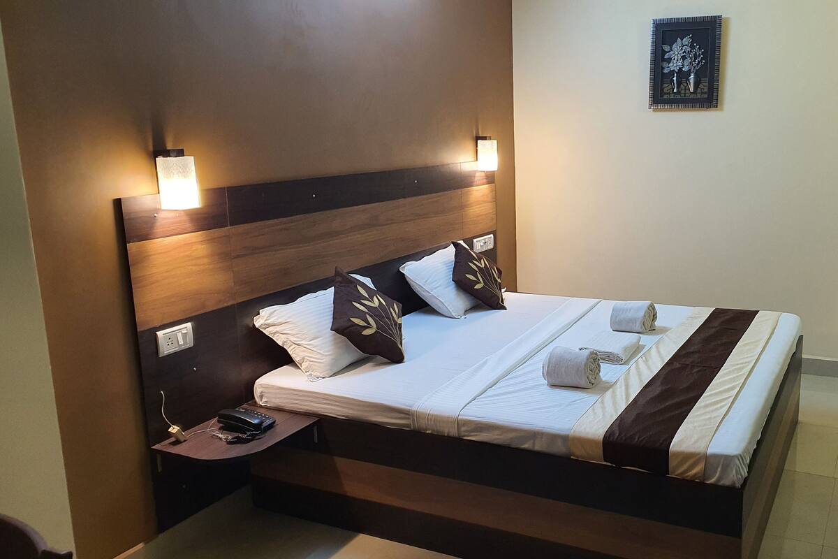 A neatly made bed with white linens and decorative pillows, a bedside table with a phone, and a wall-mounted light fixture.