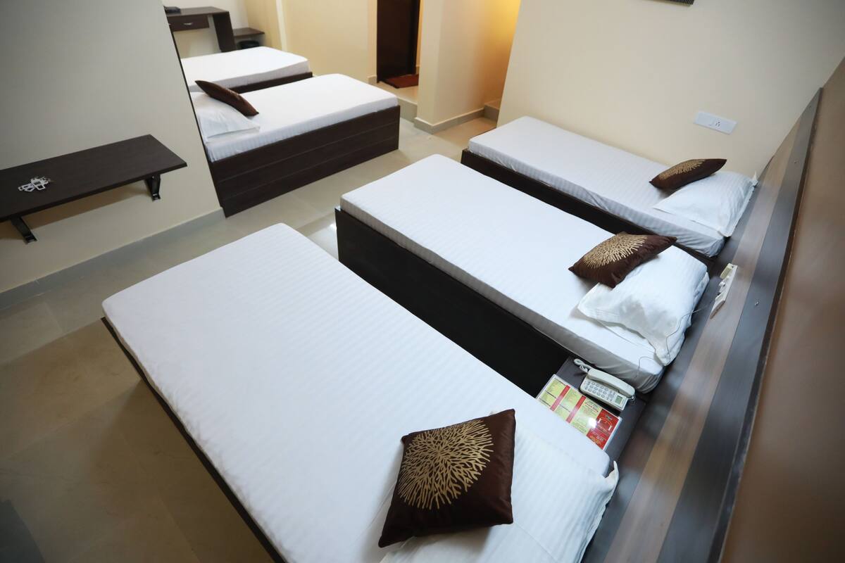 A hotel room with three single beds, each with a pillow and a bedside table.