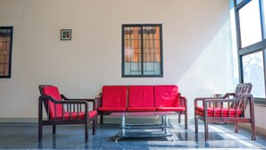 Una habitación con un sofá rojo, dos sillas de madera, una mesita y un ventanal con vistas.