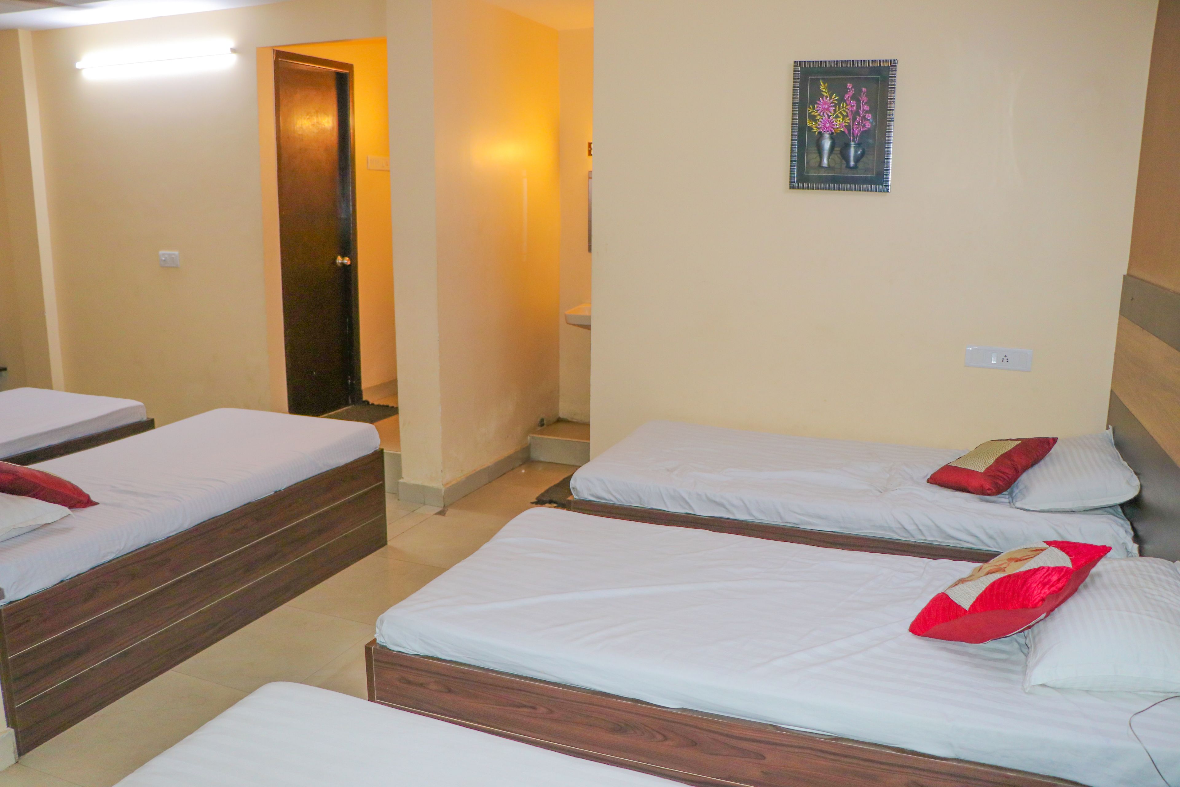 Ein Hotelzimmer mit vier Einzelbetten, jedes mit einem hölzernen Kopfteil und weißer Bettwäsche. Über den Betten hängt ein gerahmtes Bild von Blumen an der Wand.