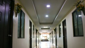 Un pasillo largo y estrecho con puertas a ambos lados, iluminación empotrada en el techo y un banco en el centro.