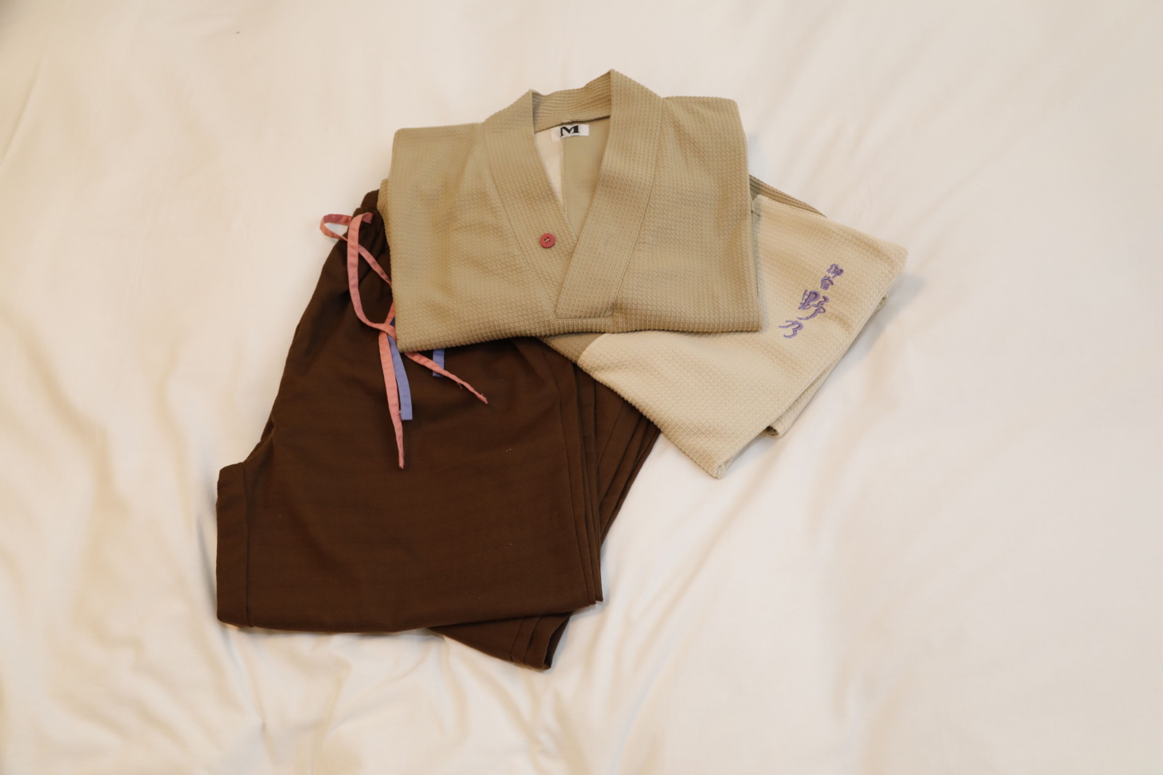 Una prenda color beige y marrón, doblada cuidadosamente sobre una cama blanca.