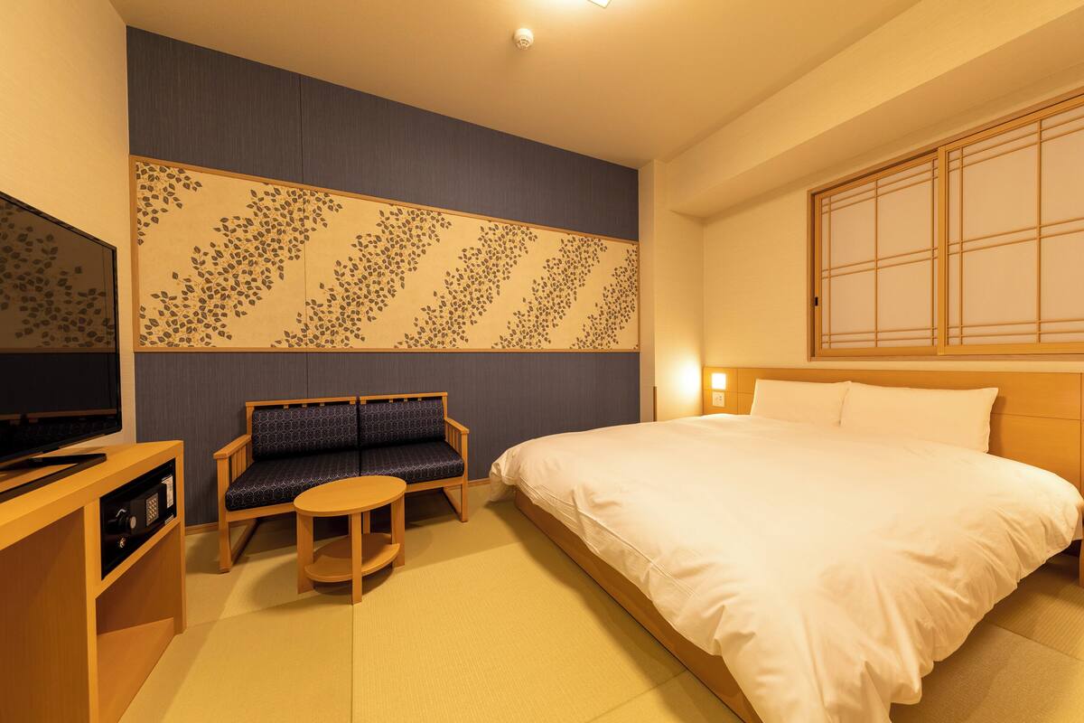 A hotel room with a bed, a sofa, a small table, and a TV.