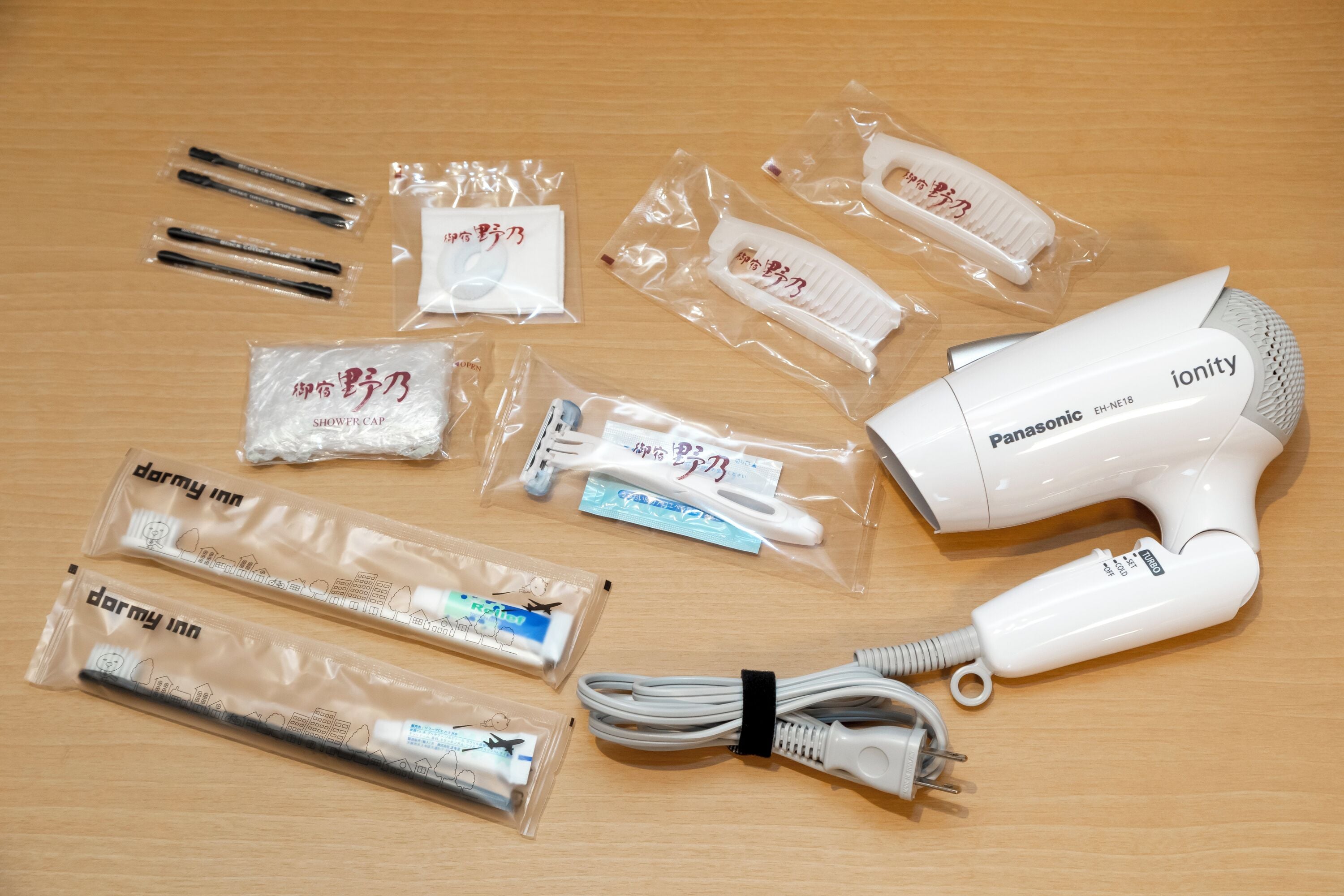 A Panasonic ionity hair dryer with its accessories, including a comb, brush, and various cables, laid out on a wooden surface.