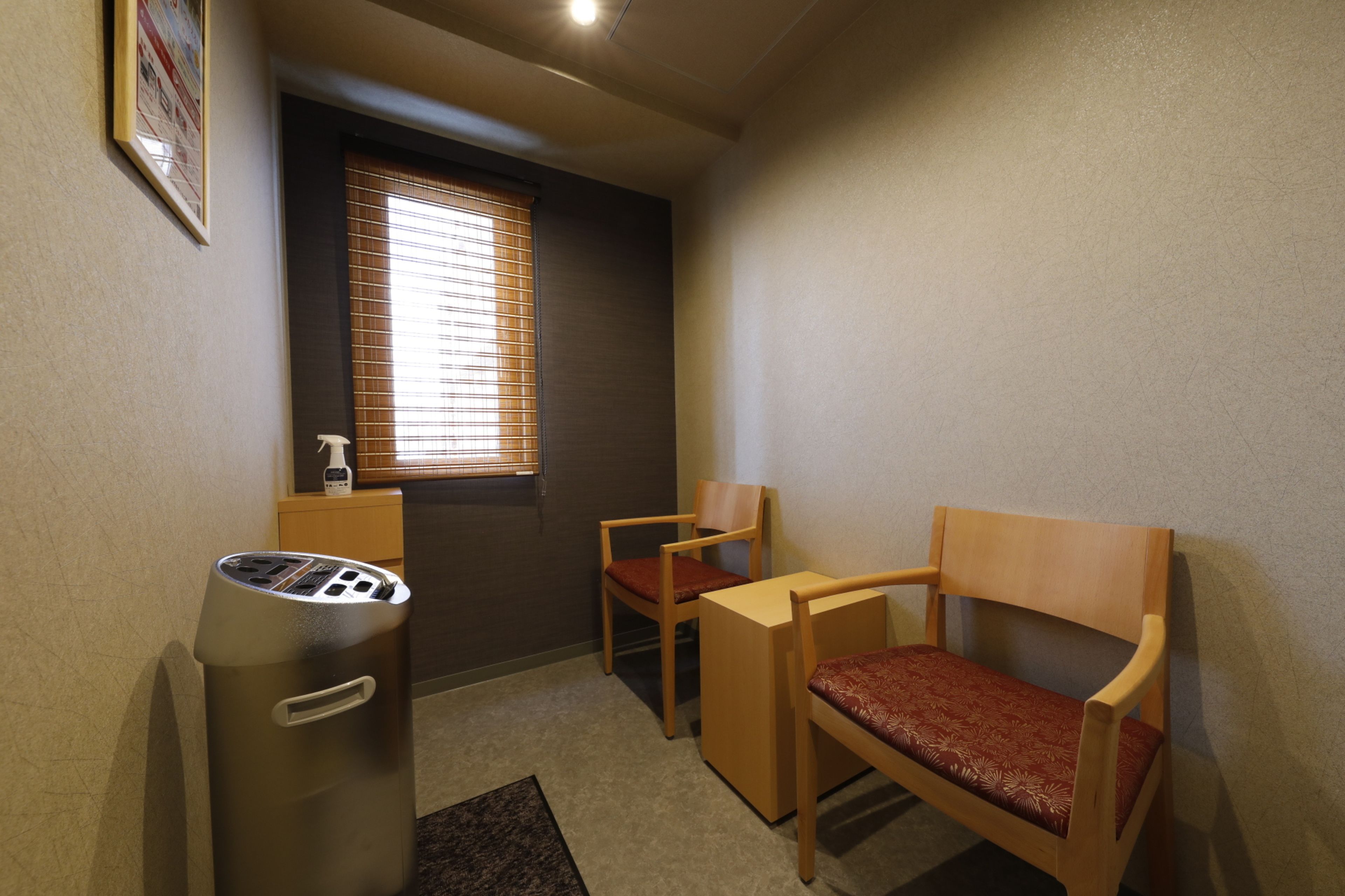 A small, private room with two wooden chairs, a small table, and a trash bin.