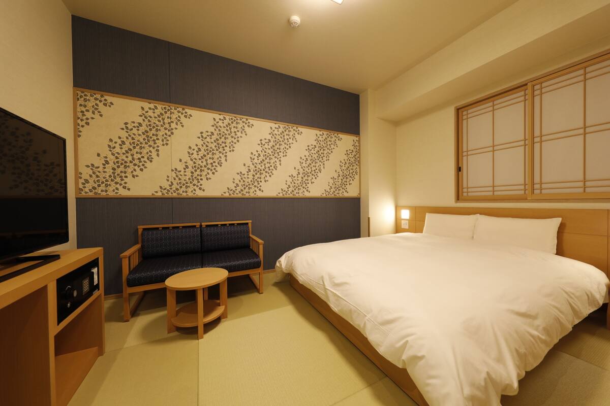 A hotel room with a bed, a sofa, a small table, and a TV.