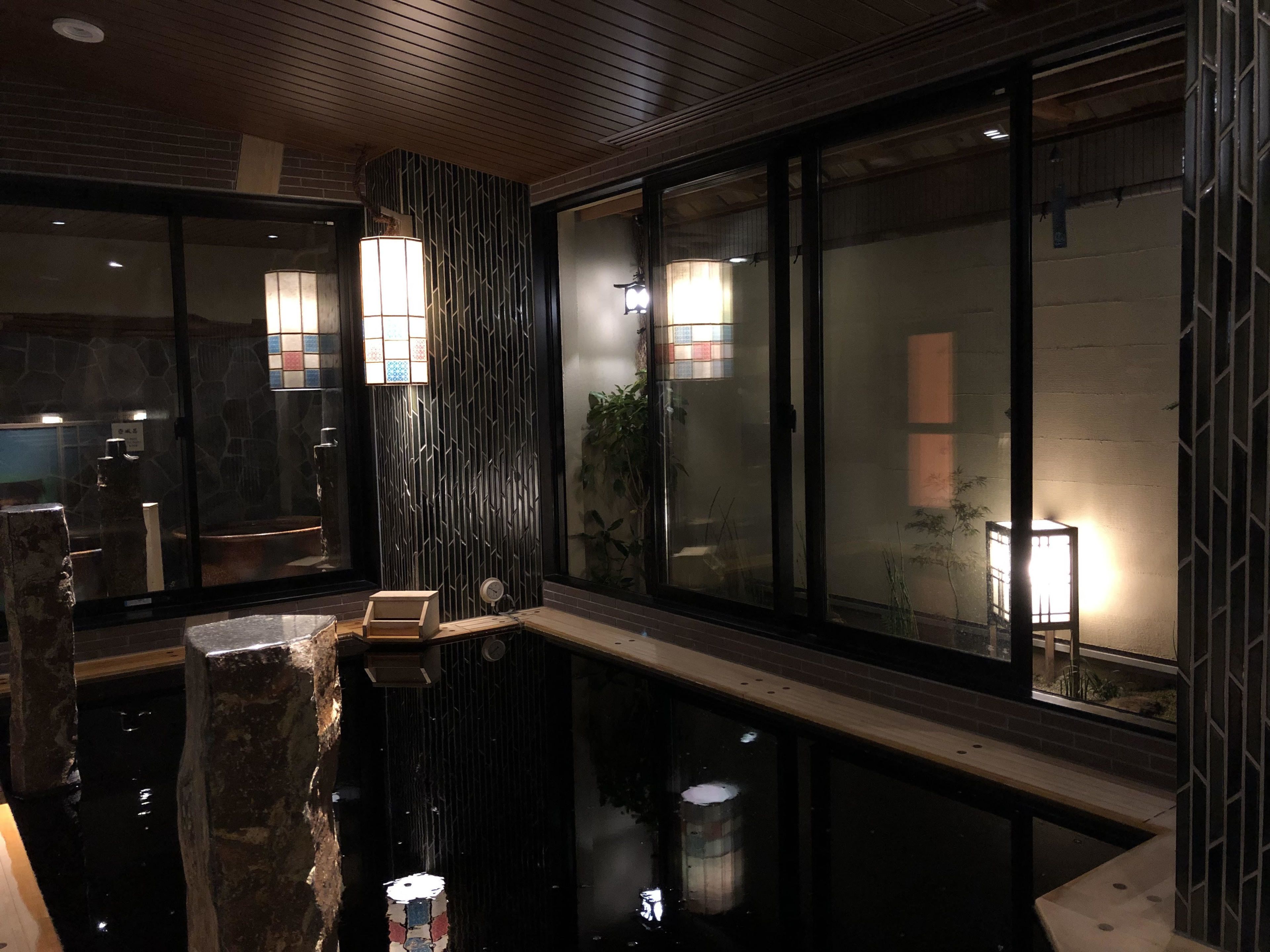 Un interior moderno con una fuente de piedra, detalles de madera y ventanas amplias con iluminación interna.