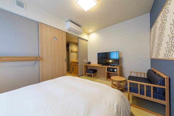 Una habitación de hotel con una cama, un escritorio con computadora, un televisor, un área de descanso y un aire acondicionado.