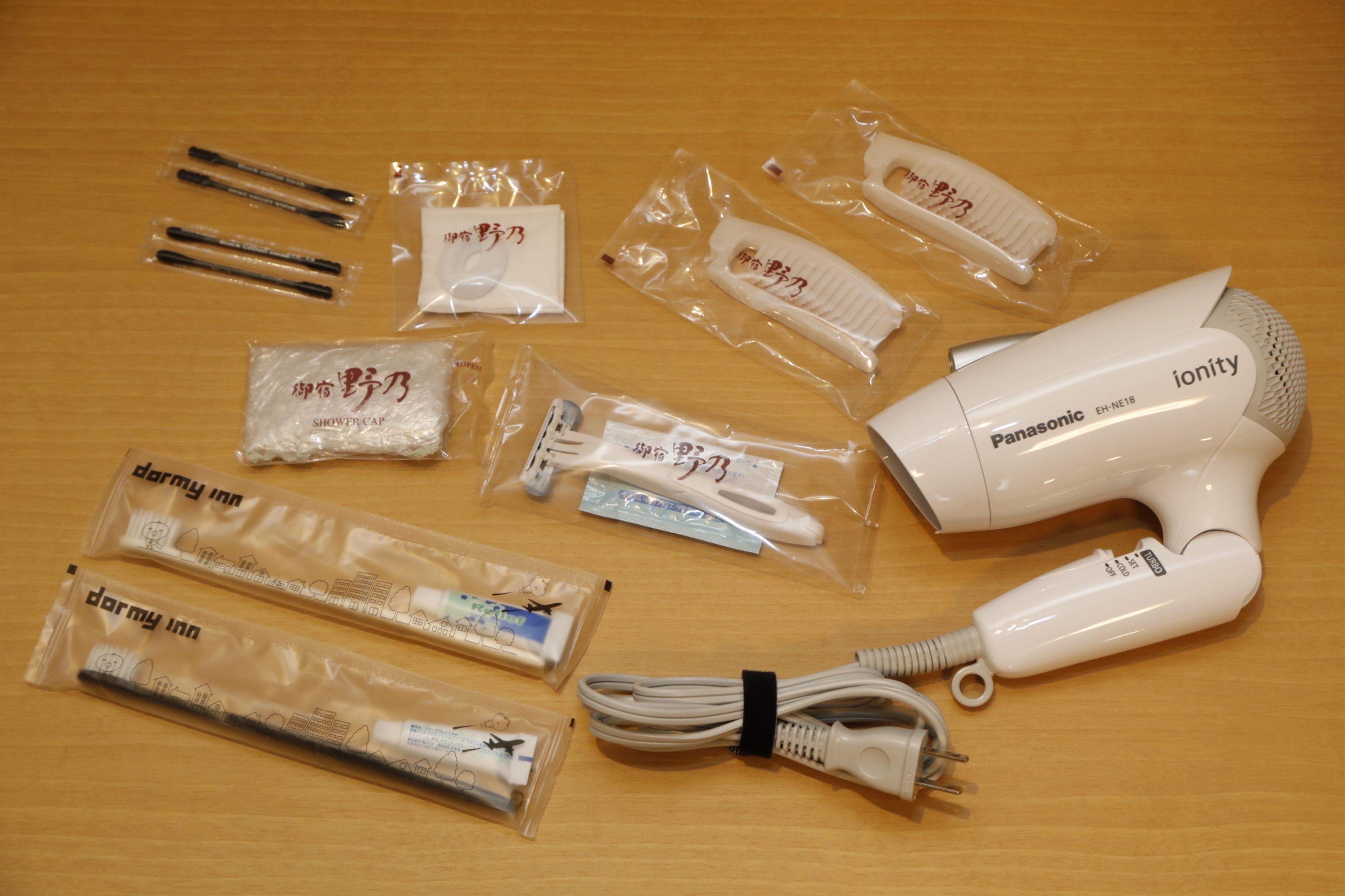 Un assecador de cabells Panasonic ionity amb els seus accessoris, com ara una escova i un cable de càrrega, damunt una superfície de fusta.