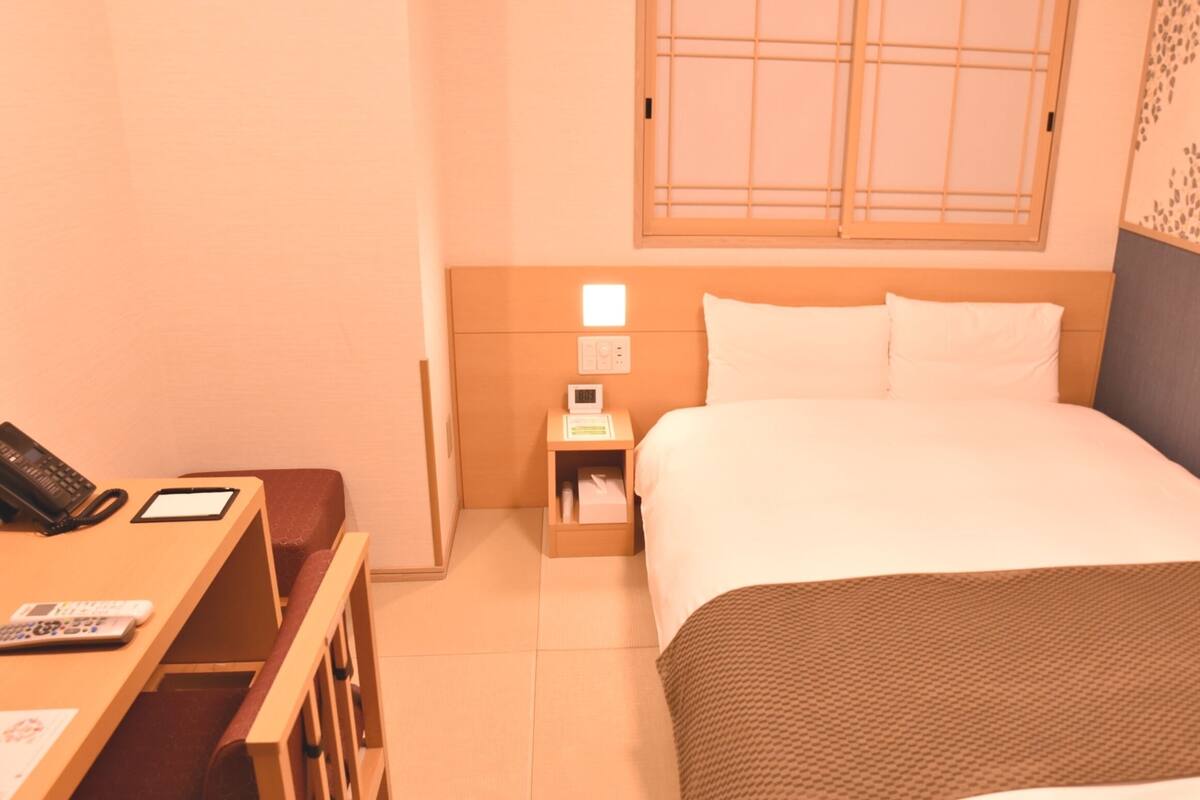 A hotel room with a bed, bedside table, lamp, and a window with a view.