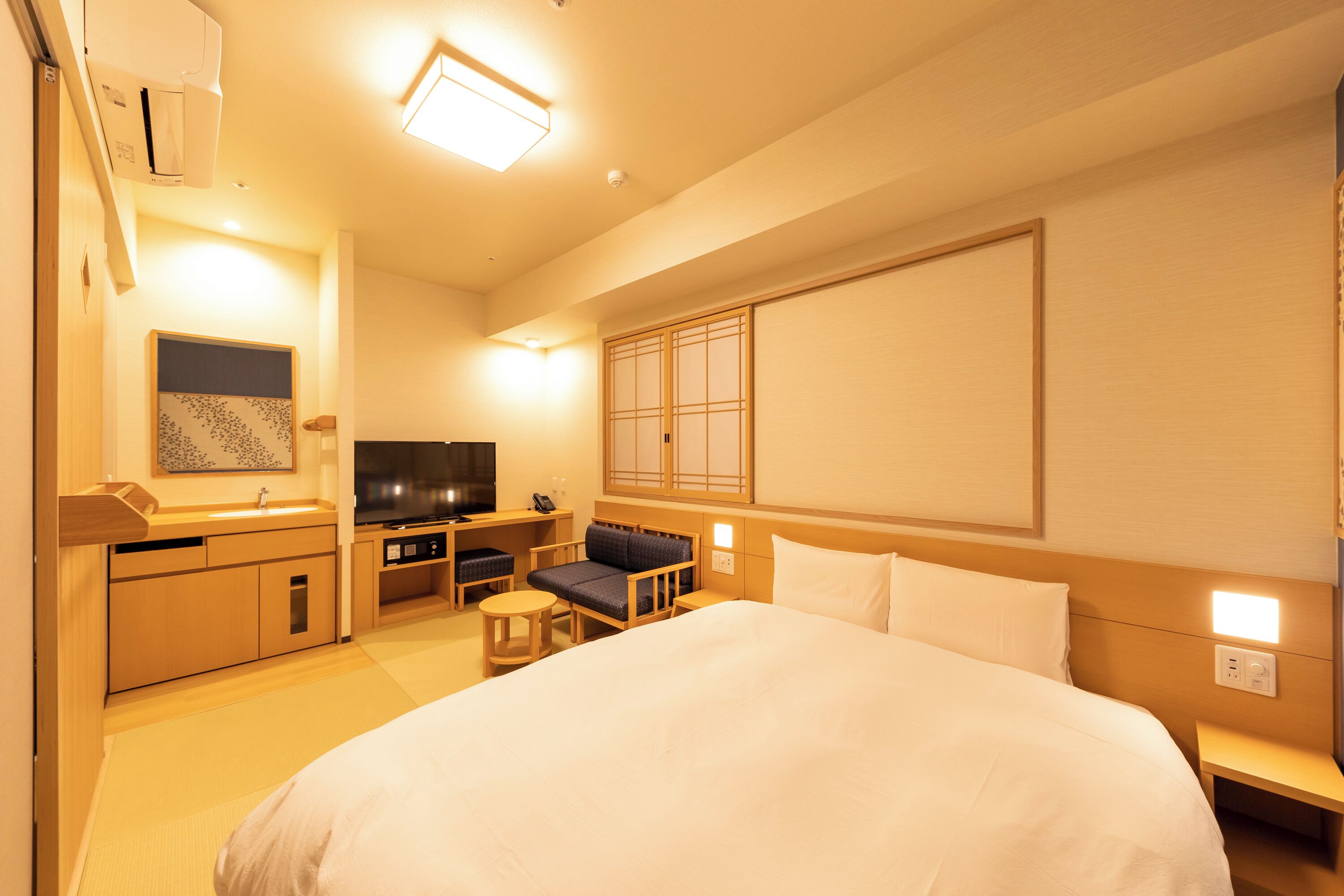 Ein Hotelzimmer mit einem großen Bett, einem Schreibtisch mit Stuhl, einem Fernseher und einem Fenster mit Aussicht.
