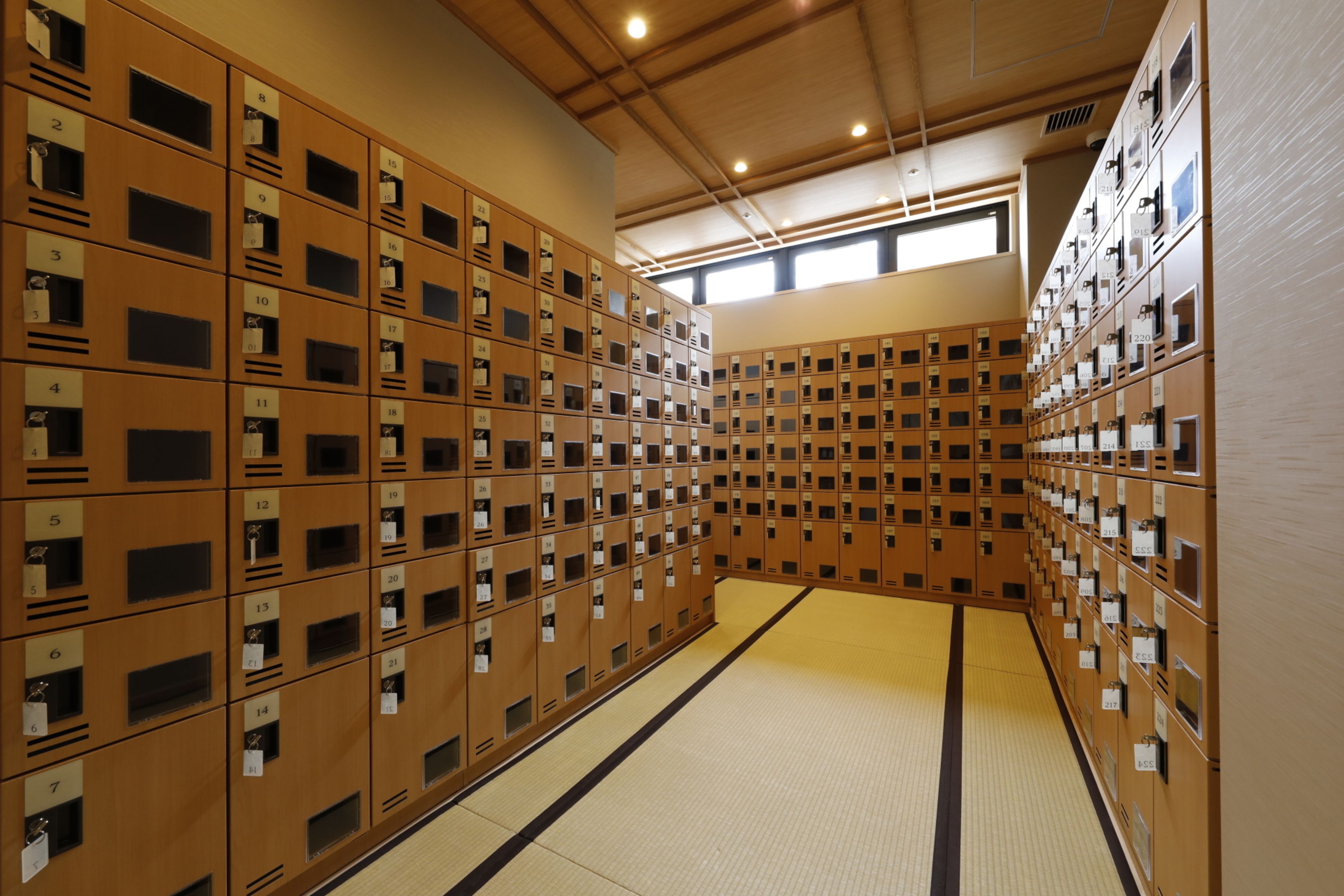 A row of wooden lockers with numbered labels, arranged in a corridor with tatami mat flooring.