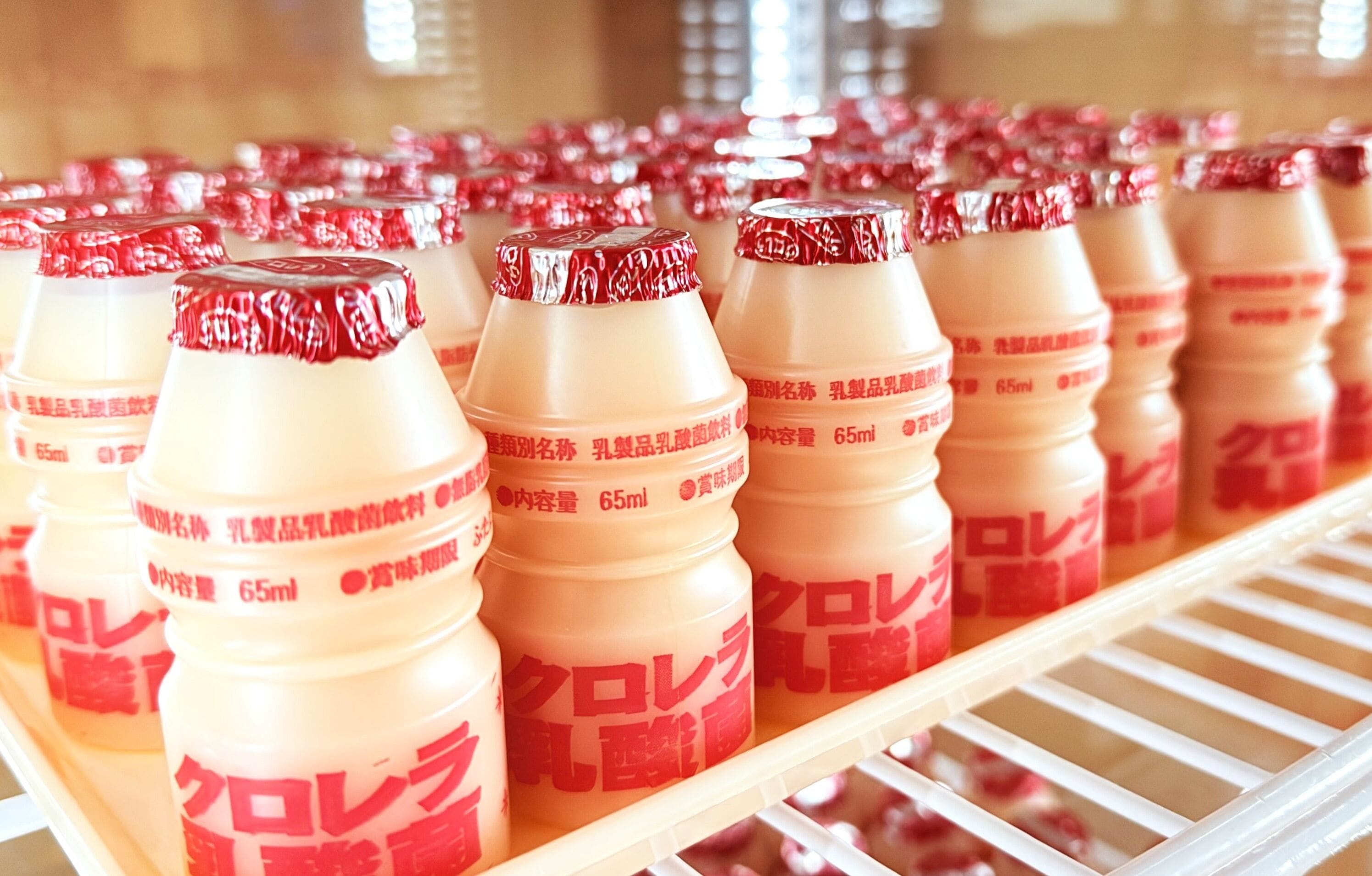 A refrigerated display shelf with multiple bottles of a beverage, each labeled with a red cap and a 65ml volume indication.