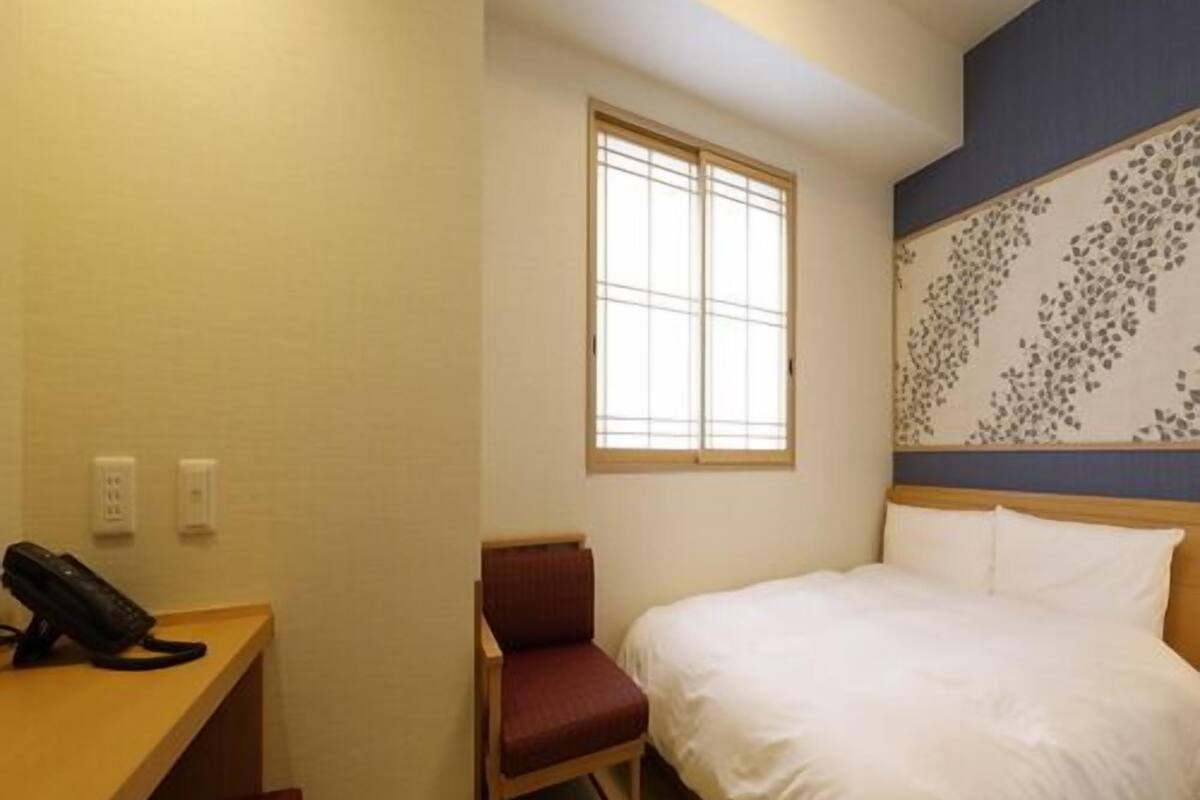 A hotel room with a bed, a desk with a telephone, a chair, and a window.