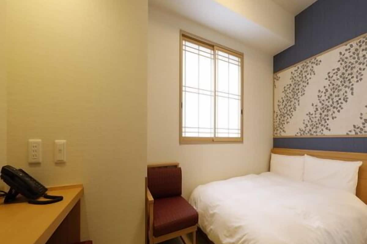 A hotel room with a bed, a desk with a telephone, a chair, and a window.