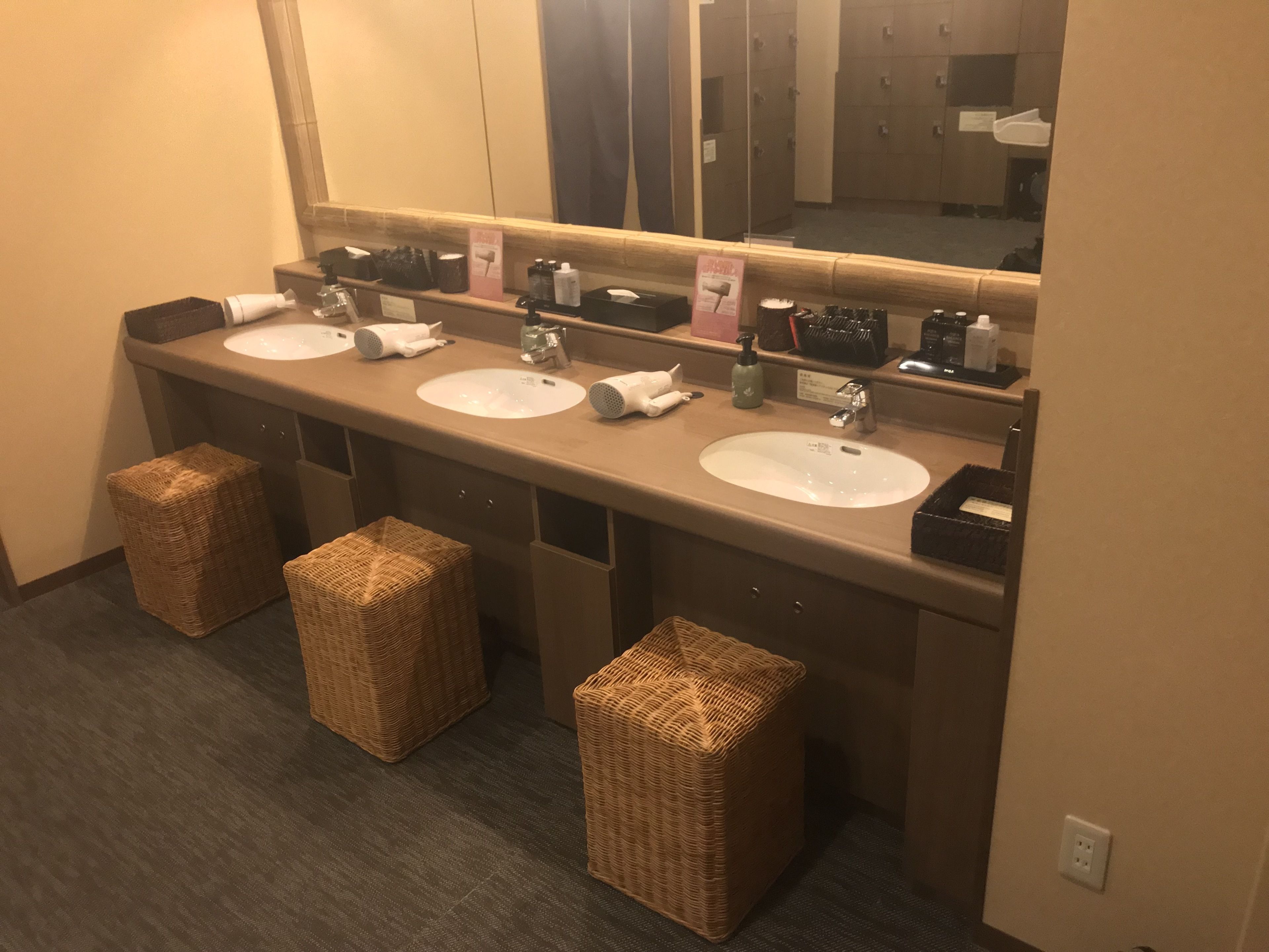 Un baño de hotel con tres lavamanos, un espejo grande y taburetes de mimbre.