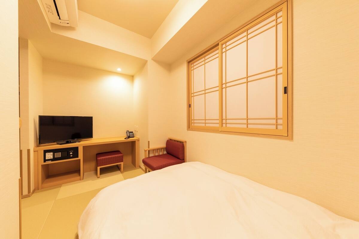 A hotel room with a bed, a TV, a desk, and a chair.