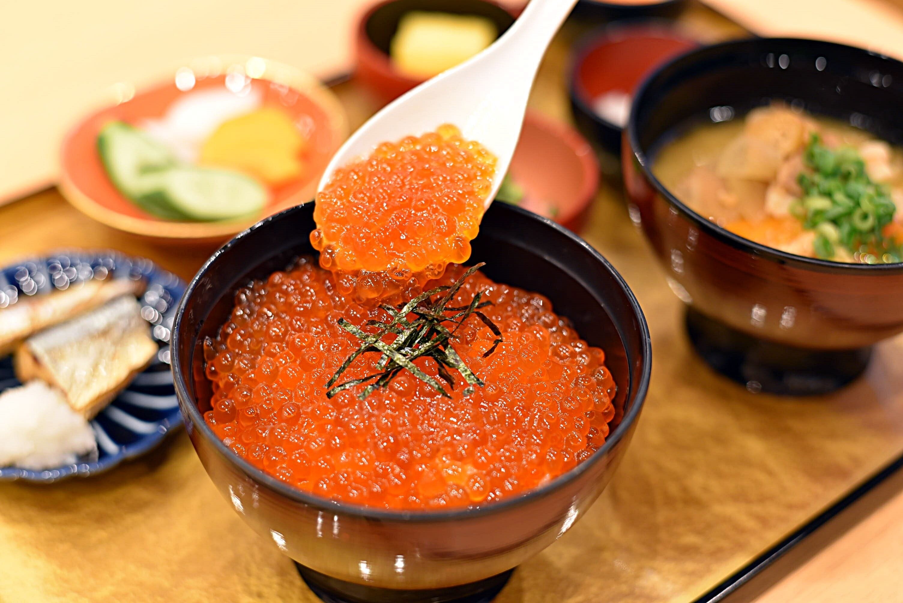 A bowl of red caviar with a spoon lifting some, surrounded by other dishes.