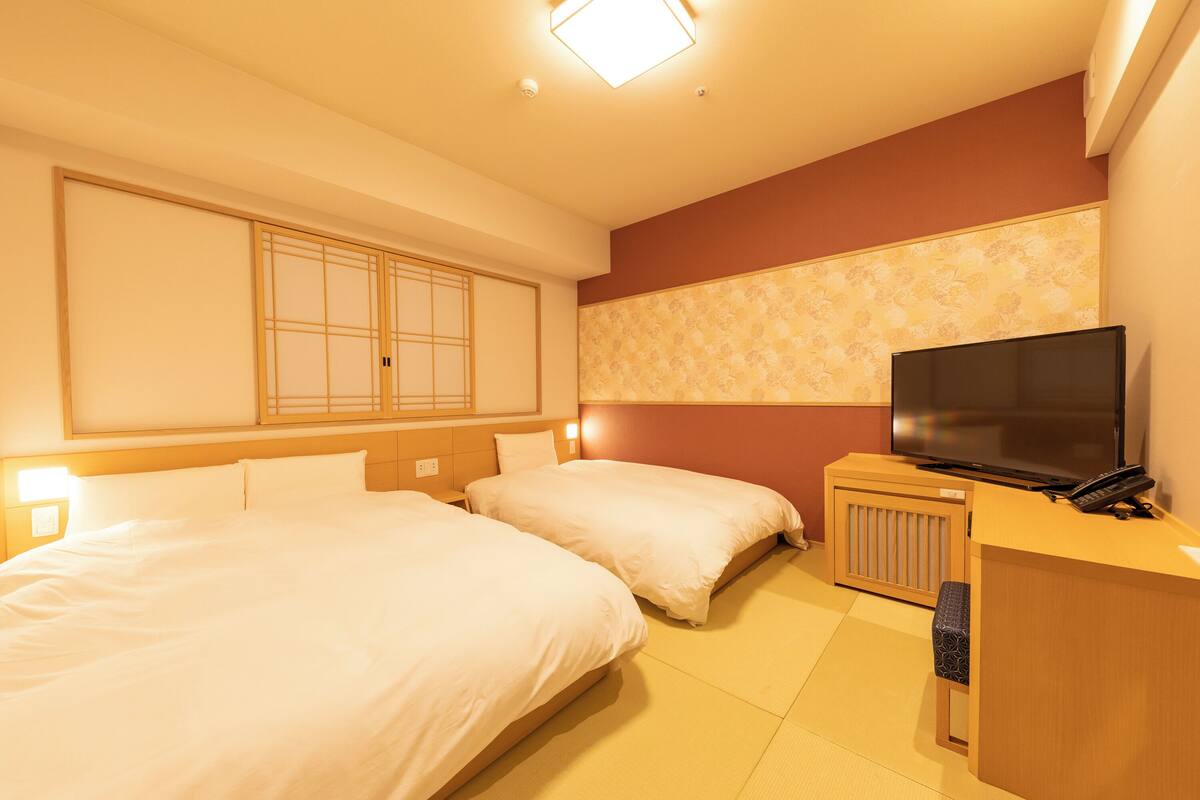 A hotel room with two beds, a TV, a desk, and a traditional sliding door.